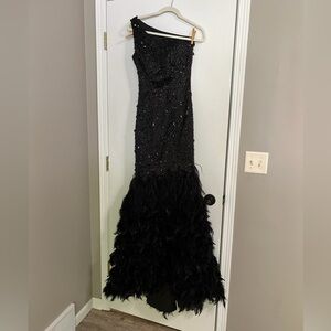 Black jeweled, one-shoulder, open back prom dress with faux feathers and slit.